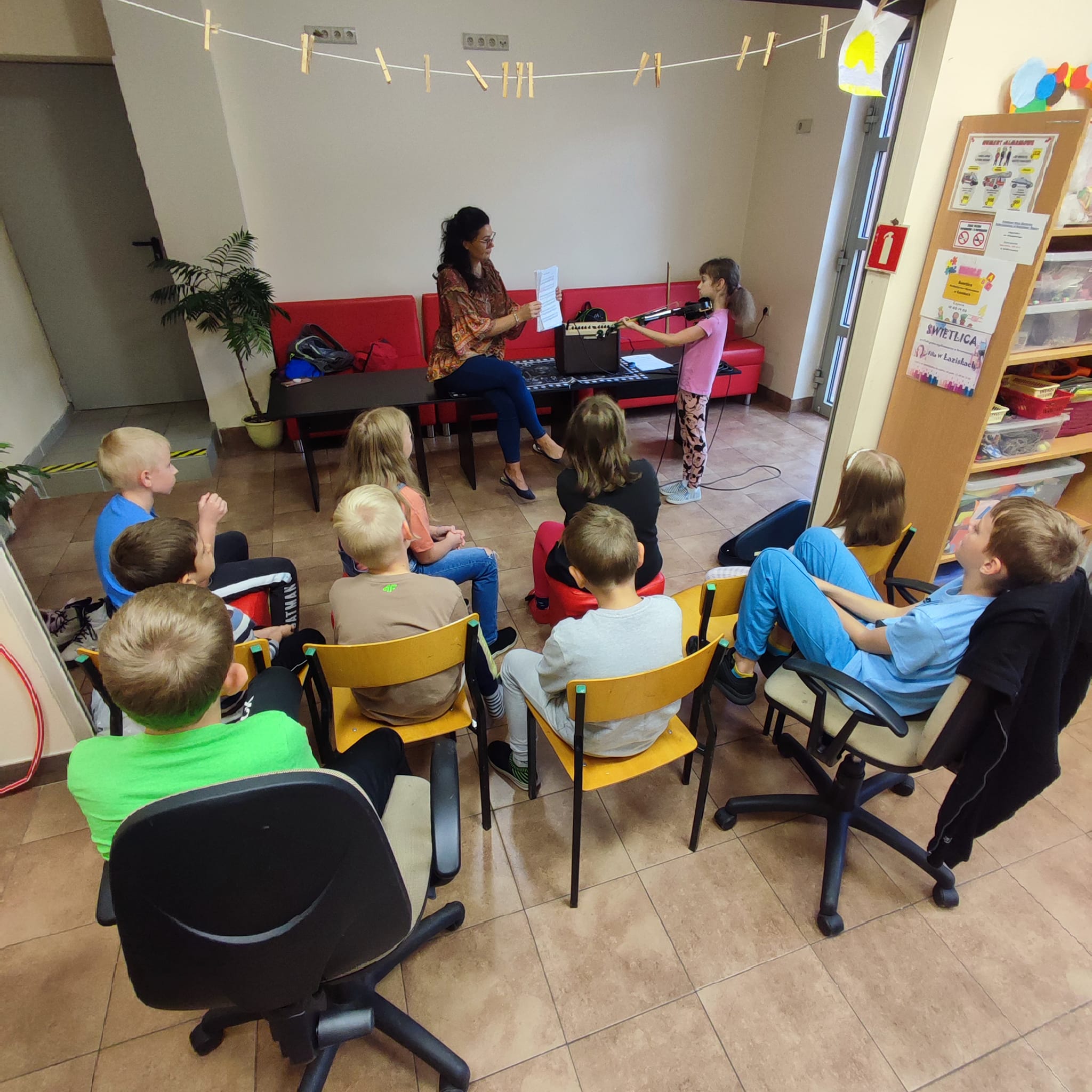 Dziewczynka gra na skrzypcach a grupa dzieci słucha muzyki
